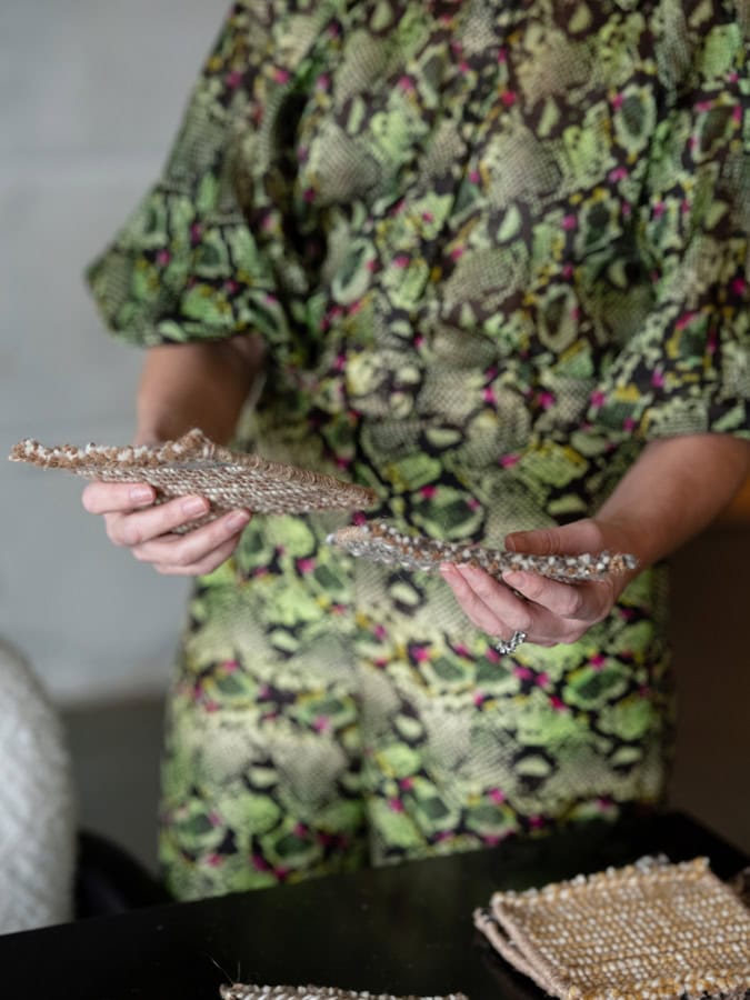 Photo by Florence Charvin Photography of A person wearing a green snakeskin-patterned outfit holds two textured, beaded fabric samples over a table.
