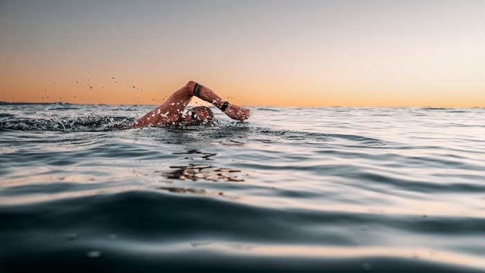 Photo by Florence Charvin Photography of A person swims in open water at sunset, with one arm extended forward above the surface and gentle waves surrounding them.